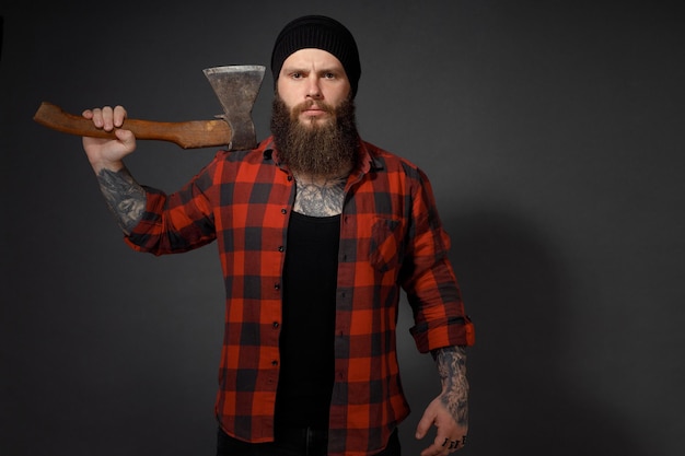 Gut aussehender Mann mit langen Haaren mit einer Axt in den Händen auf dunklem Studiohintergrund.