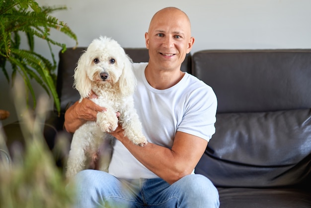 Gut aussehender Mann mit süßem weißen Hund zu Hause auf dem Sofa