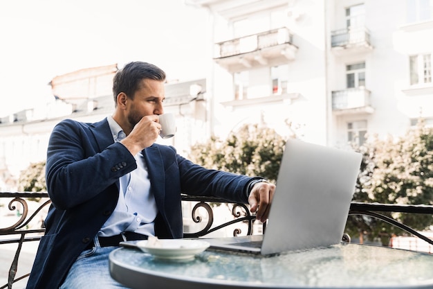 Gut aussehender Mann mit Tasse Kaffee arbeitet online mit Laptop im Café. Heimarbeit.