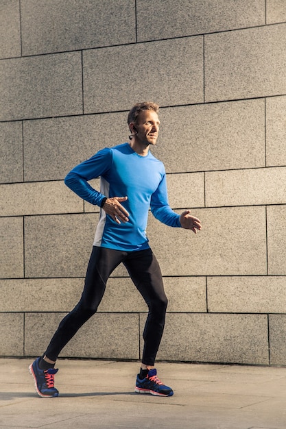 Gut aussehender Mann mittleren Alters in blau-schwarzer Sportuniform und Kopfhörer und Fitness-Tracker ist