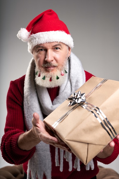 Gut aussehender Mann mittleren Alters mit verziertem Bart mit Weihnachtsmütze, der die Kamera ausgestreckt anschaut