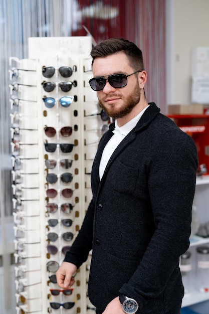 Gut aussehender Mann Modell wählt Mode-Sonnenbrille in Optik. Breites Sortiment an modernen Brillen im Shop.