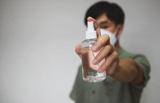 Gut aussehender Mann setzte eine Maske mit Alkoholsprühflasche für Hygienereiniger Coronavirus auf