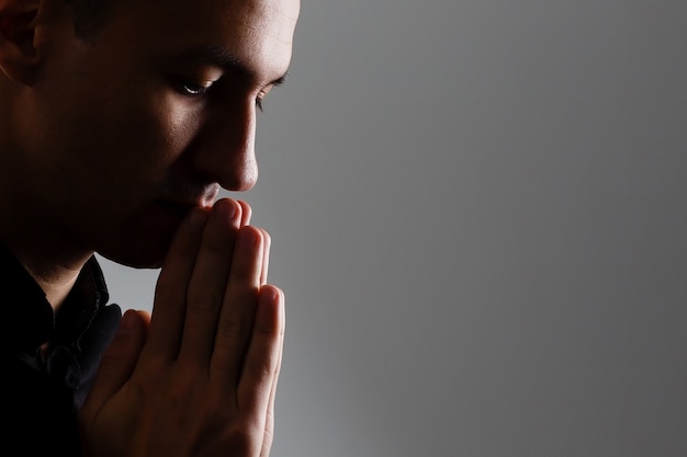 Gut aussehender Mann sitzt Gebet auf schwarzem Hintergrund. Seine Hände beten um Gottes Segen.