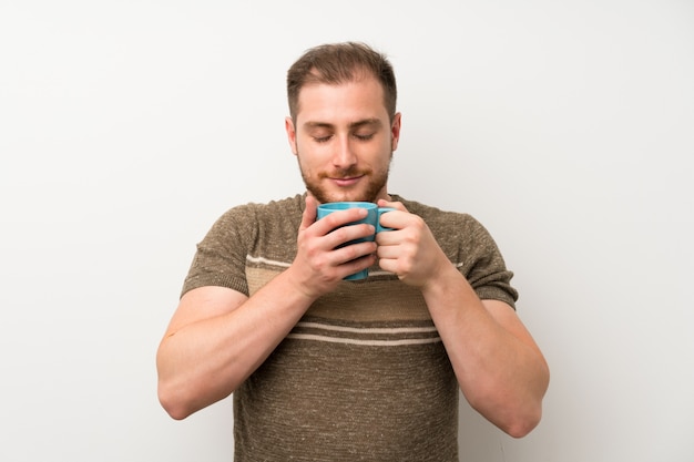 Gut aussehender Mann über der lokalisierten weißen Wand, die heißen Tasse Kaffee hält