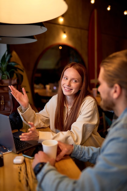 Gut aussehender Mann und positive Rothaarige, die beim Kaffeetrinken Geschäftsprojekte im Café besprechen. In der gemütlichen Cafeteria. Startup, Ideen und Brainstorming-Konzept. Seitenansicht. Platz kopieren