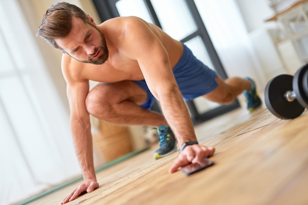 Foto gut aussehender muskulöser mann, der sport macht und online-training auf dem handy ansieht