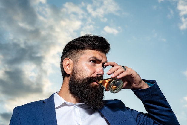 Gut aussehender nachdenklicher Mann hält ein Glas Whisky und schaut im Freien weg