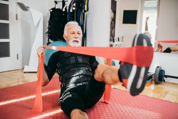 Gut aussehender und positiver älterer Mann, der Übungen im Anzug zur elektrischen Muskelstimulation macht.