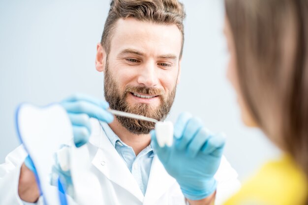 Foto gut aussehender zahnarzt, der eine patientin berät, die zahnmodell in der zahnarztpraxis hält