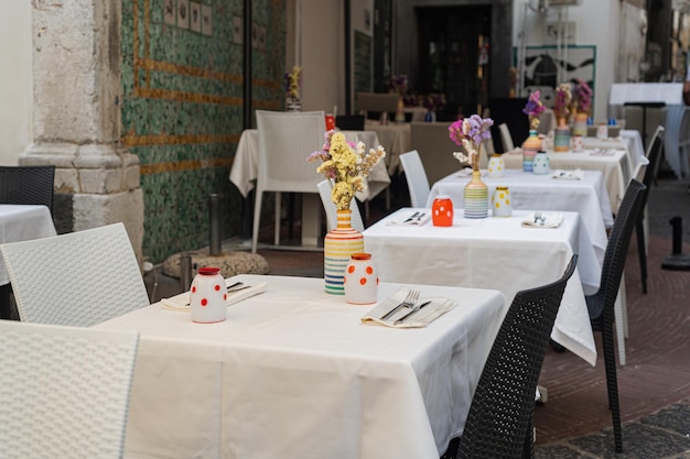 Gut bediente Tische in einem Café-Restaurant frische bunte Blumen in Vasen weiße Tischdecken Sommerterrasse Urlaub in Italien