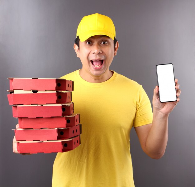 gutaussehender asiatischer Mann in der gelben Kappe, die italienische Pizza der Lebensmittelbestellung in den Pappkartons lokalisiert gibt, die im Studio lokalisiert werden.