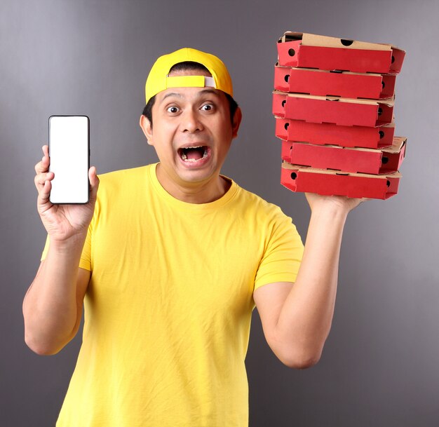 gutaussehender asiatischer Mann in der gelben Kappe, die italienische Pizza der Lebensmittelbestellung in den Pappkartons lokalisiert gibt, die im Studio lokalisiert werden.