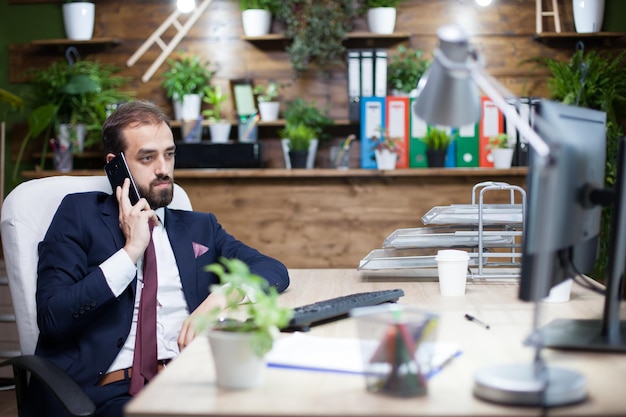 Gutaussehender bärtiger Geschäftsmann im Anzug unterhält sich auf seinem Handy. Eleganter Geschäftsmann in seinem Büro.