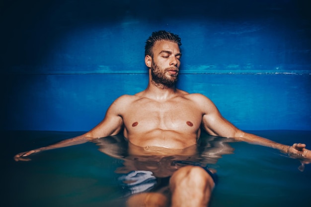 Gutaussehender Bartmann, der in einem Tank schwimmt, der mit dichtem Salzwasser gefüllt ist, das in Meditation, Therapie und alternativer Medizin verwendet wird.