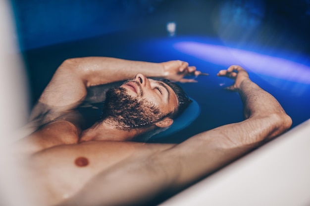 Gutaussehender Bartmann, der in einem Tank schwimmt, der mit dichtem Salzwasser gefüllt ist, das in Meditation, Therapie und alternativer Medizin verwendet wird.