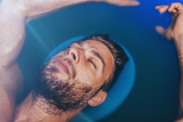 Gutaussehender Bartmann, der in einem Tank schwimmt, der mit dichtem Salzwasser gefüllt ist, das in Meditation, Therapie und alternativer Medizin verwendet wird.