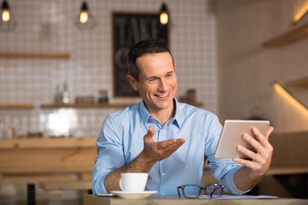 Gutaussehender Geschäftsmann, der mit jemandem per Videochat über ein digitales Tablet im Café spricht