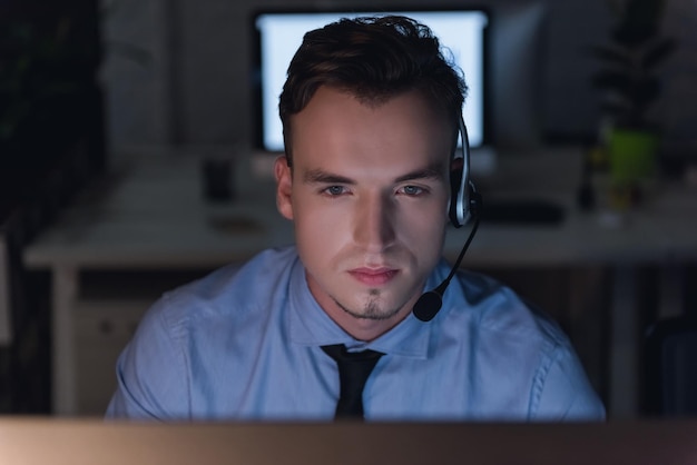 Gutaussehender Geschäftsmann mit Headset arbeitet spät in der Nacht mit einem Computer im Büro