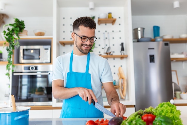 Gutaussehender junger Mann steht an der modernen Küche, hackt Gemüse, bereitet frischen Gemüsesalat zum Abendessen oder Mittagessen zu, junger Mann, der zu Hause kocht