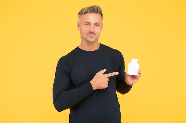 Gutaussehender Kerl im lässigen Stil zeigt mit dem Zeigefinger, der Herrenparfümerieprodukte für die Pflege und Körperpflege auf gelbem Hintergrund präsentiert