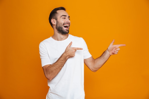 gutaussehender Kerl im T-Shirt, der Finger im Stehen beiseite zeigt, isoliert auf Gelb