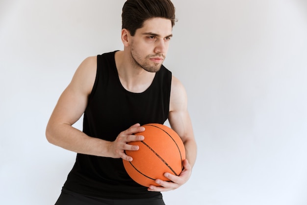 gutaussehender konzentrierter ernster starker junger Sportmann-Basketballspieler, der Ball isoliert hält.