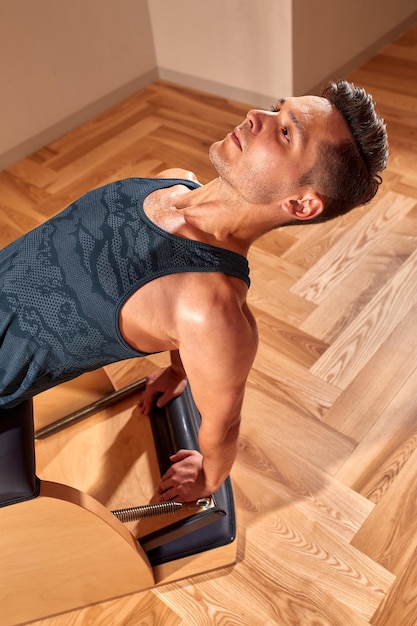 Gutaussehender männlicher Pilates-Trainer, der im modernen Innenbereich des Pilates-Studios Stretching-Balance-Fitnessübungen auf kleinen Laufgeräten durchführt