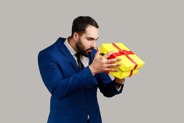 Gutaussehender Mann, der das Geschenk auspackt und in die Schachtel schaut, mit neugierigem, ernstem Gesichtsausdruck