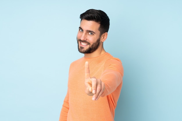 gutaussehender Mann, der einen Finger über isoliertem Blau zeigt und hebt
