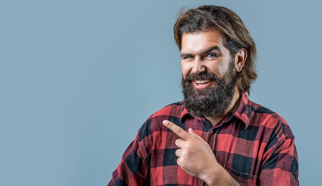 Gutaussehender Mann mit breitem Lächeln im Gesicht, der mit Hand und Finger zur Seite zeigt. Porträt eines attraktiven, fröhlichen Managers, der isoliert auf grauem Hintergrund Werbeflächen vorführt