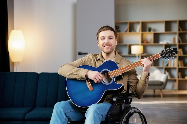 Gutaussehender Mann mit einer Behinderung sitzt im Rollstuhl und spielt zu Hause Gitarre