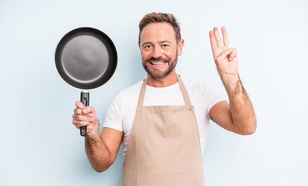 Gutaussehender Mann mittleren Alters, der freundlich lächelt und aussieht und Nummer drei zeigt. Bratpfannenkonzept