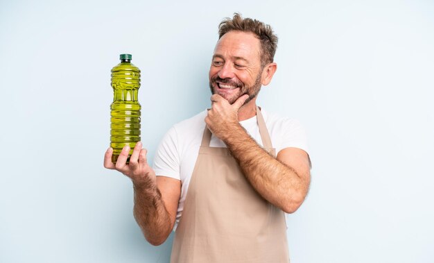Gutaussehender Mann mittleren Alters, der mit einem glücklichen, selbstbewussten Ausdruck mit der Hand am Kinn lächelt. Olivenöl Konzept