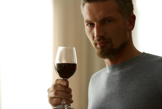 Foto gutaussehender mann mittleren alters, der rotwein in der nähe probiert