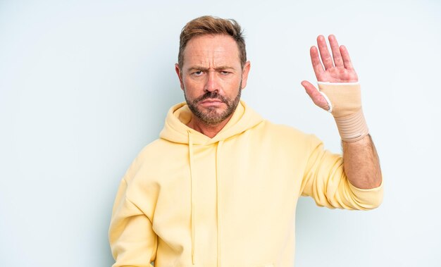 Gutaussehender Mann mittleren Alters, der sich traurig und weinerlich mit einem unglücklichen Blick und Weinen fühlt. Konzept der gebrochenen Hand