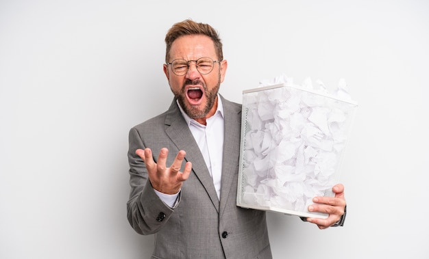 Gutaussehender Mann mittleren Alters, der wütend, verärgert und frustriert aussieht, Papierkugeln-Trash-Konzept