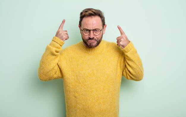 Gutaussehender Mann mittleren Alters mit einer schlechten Einstellung, die stolz und aggressiv aussieht, nach oben zeigt oder mit den Händen lustige Zeichen macht