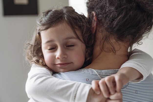 Gute Familienmutter und Tochter Kleine Tochter umarmt ihre Mutter mit einem Lächeln und geschlossenen Augen zu Hause