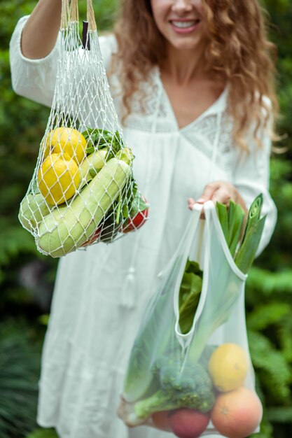 Gute Laune. Frau im weißen Kleid, das Taschen mit verschiedenem Gemüse trägt und sich fröhlich fühlt