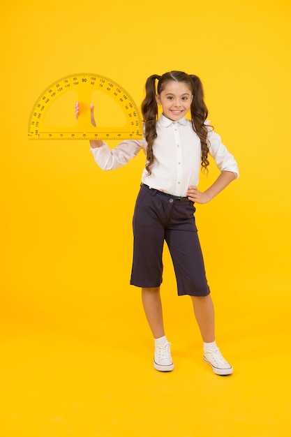 Gute Leistung in Mathe Nettes kleines Schulmädchen, das Messwerkzeug für Mathematik auf gelbem Hintergrund hält Kleines Kind mit Winkelmesser für den Mathematikunterricht Grundschule Mathematik oder Mathematik