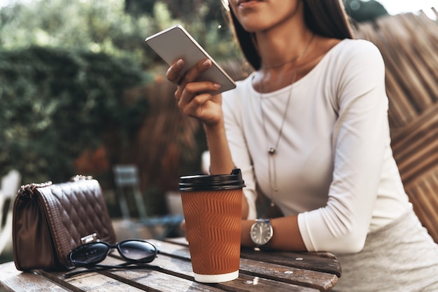 Gute Rückmeldungen erhalten. Nahaufnahme einer jungen Frau, die ein Smartphone hält, während sie im Restaurant im Freien sitzt