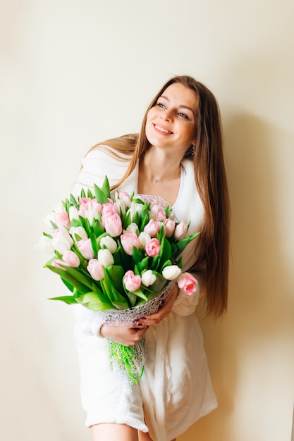 Guten Morgen! Attraktive junge Frau mit langen Haaren und Strauß weißer und rosa Tulpen verbringt Zeit zu Hause.