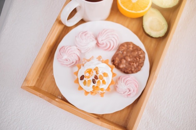 Guten Morgen. Frühstück im Bett mit Orange, Avocado, Kuchen, Marshmallows, Schokoladenkeksen im Holztablett. Lifestyle, Essen, Essen, Wohnkomfort und Entspannungskonzept