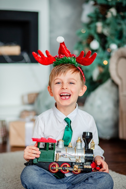 Guten Morgen. Glücklicher kleiner Junge mit einem Geschenk, Spielzeugzug, unter dem Weihnachtsbaum. Zeit, Wünsche zu erfüllen.