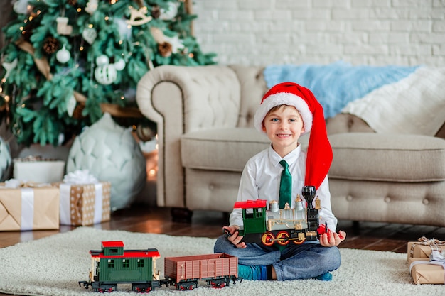 Guten Morgen. Glücklicher kleiner Junge mit einem Geschenk, Spielzeugzug, unter dem Weihnachtsbaum. Zeit, Wünsche zu erfüllen.