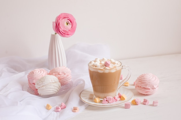 Guten Morgen Karte in rosa. Eine Tasse Kaffee, ein Marshmallow und eine rosa Blume auf einem hellen Holzplatz.