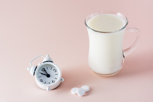 Guter Schlaf. Ein Glas Milch ein Produkt zum guten Einschlafen, Schlaftabletten und ein Wecker auf einem rosa Hintergrund. Abendritual