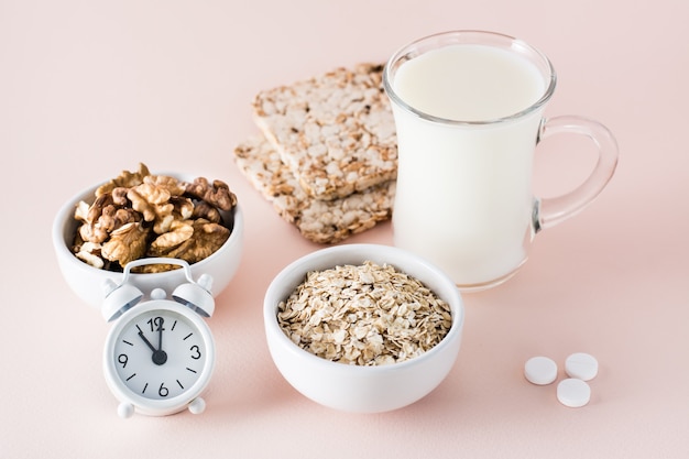 Guter Schlaf. Lebensmittel für guten Schlaf - Milch, Walnüsse, Knäckebrot, Haferflocken, Schlafpille und Wecker auf rosa Hintergrund