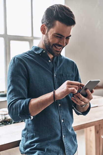 Gutes Feedback vom Kunden. Hübscher junger Mann, der Smartphone benutzt und lächelt